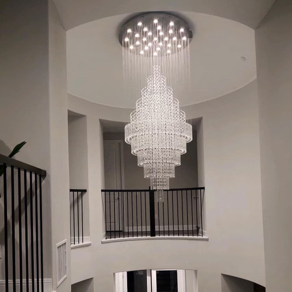 Elegant modern chandelier hanging from a ceiling in a spacious foyer with a curved balcony.