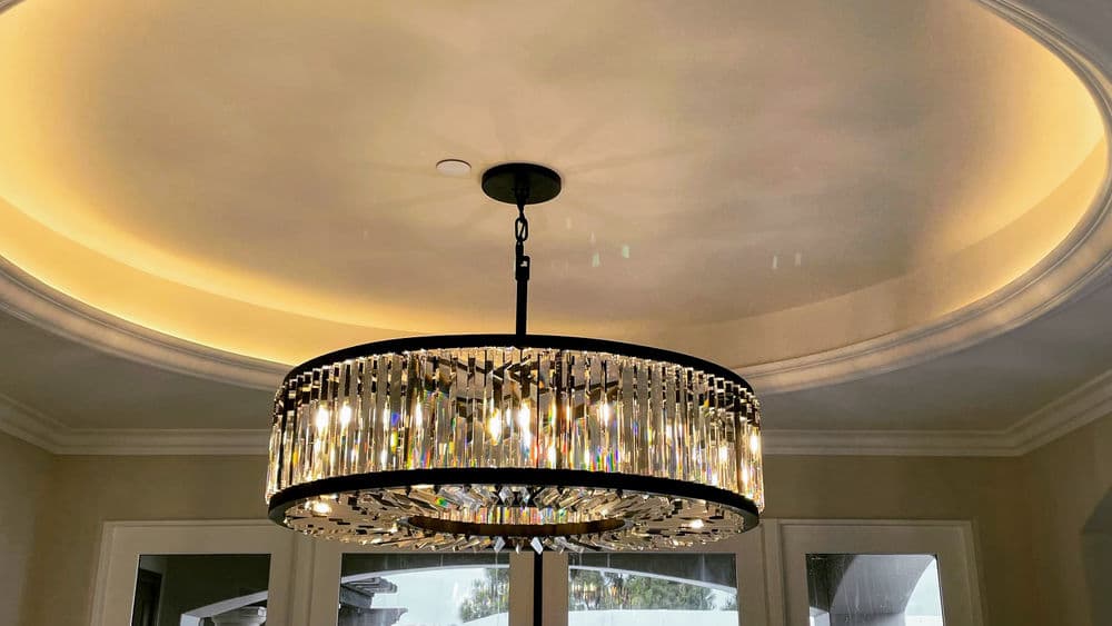 Elegant crystal chandelier hanging from a coffered ceiling with soft ambient lighting.