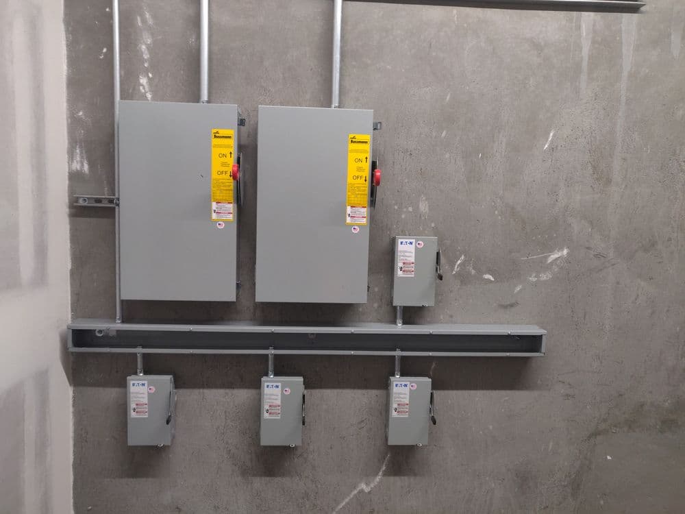 Electrical control panels mounted on a concrete wall with safety labels in a utility room.
