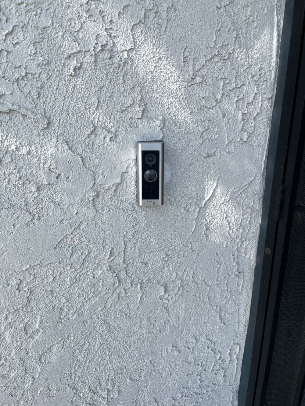 Modern video doorbell installed on textured white exterior wall.