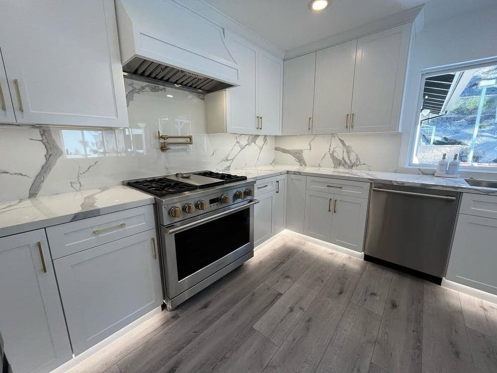 Modern kitchen with white cabinets, marble backsplash, stainless steel appliances, and wood flooring.