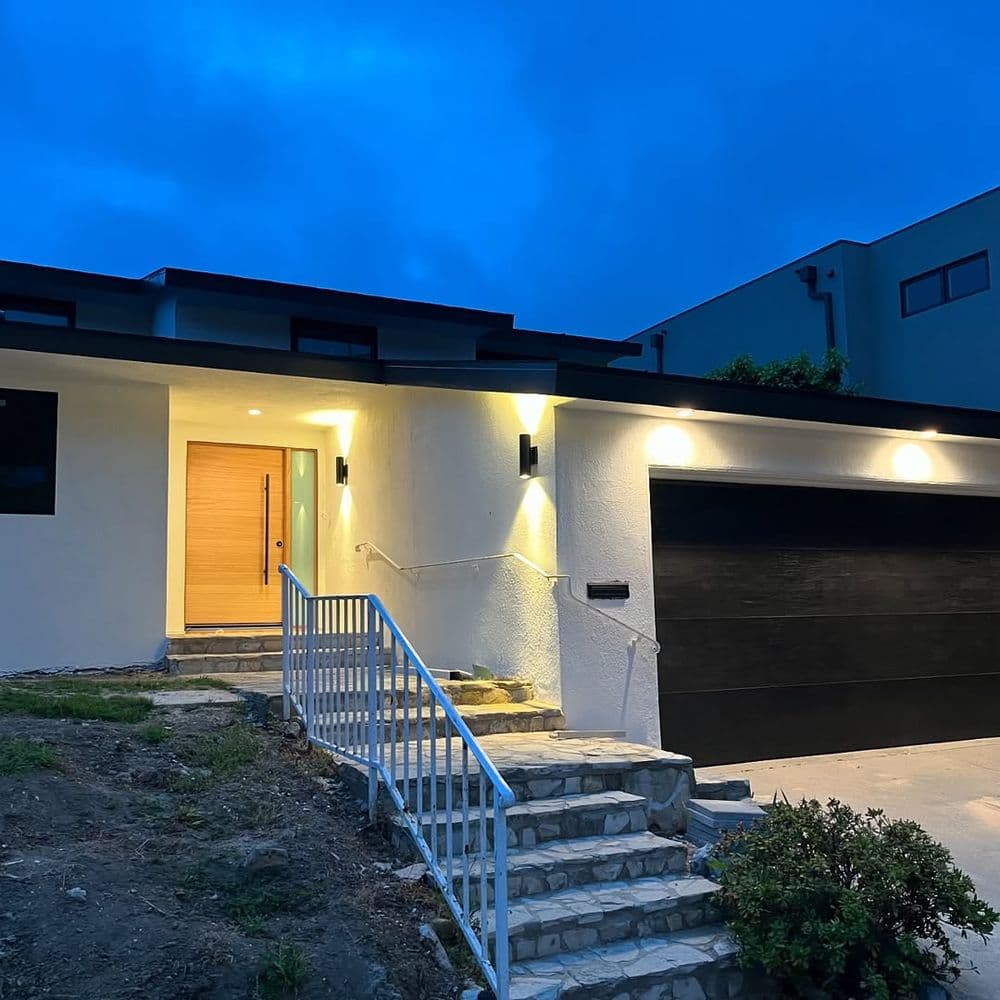 Modern exterior of a house with illuminated entrance and stone steps at dusk.